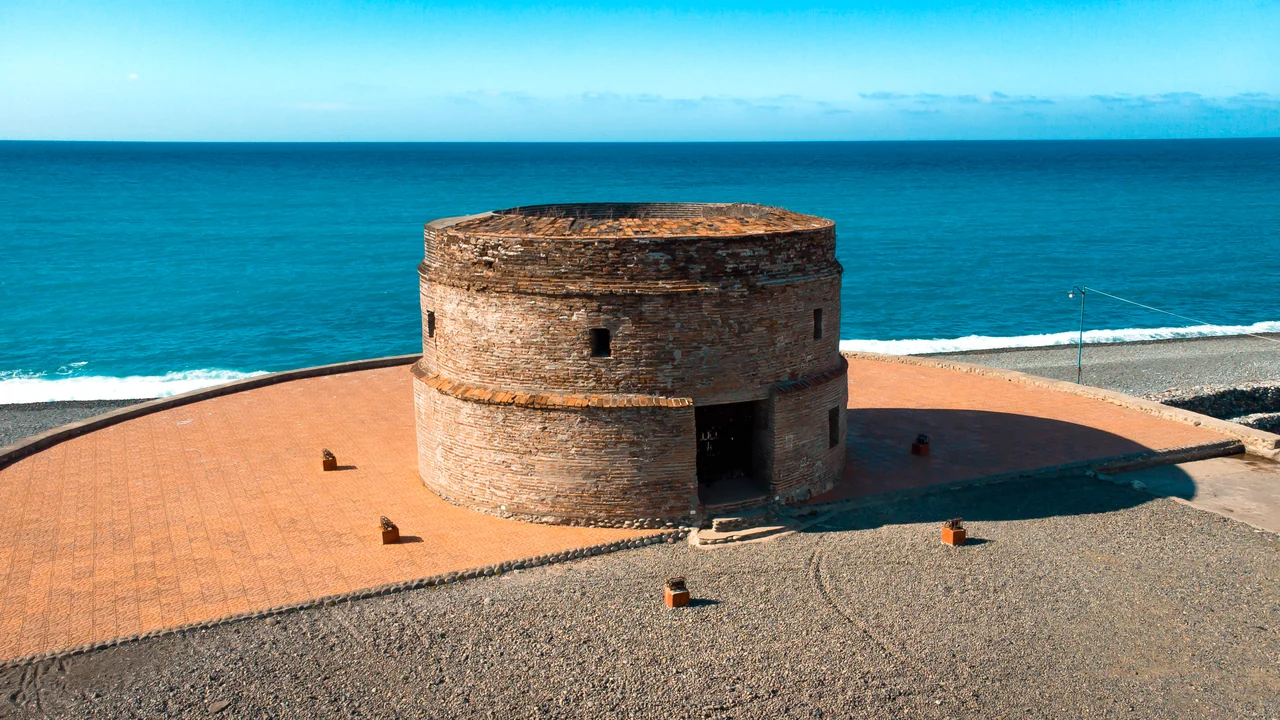 The round brick Baluarte Watchtower beside Luna’s pebble shore and blue sea